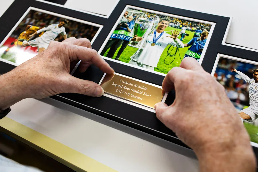 An engraved plaque being fitted into a mount beneath signed photos