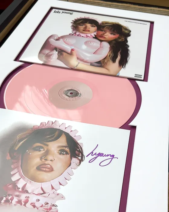A Lola Young record framed with its sleeve, the pink vinyl and a signed print