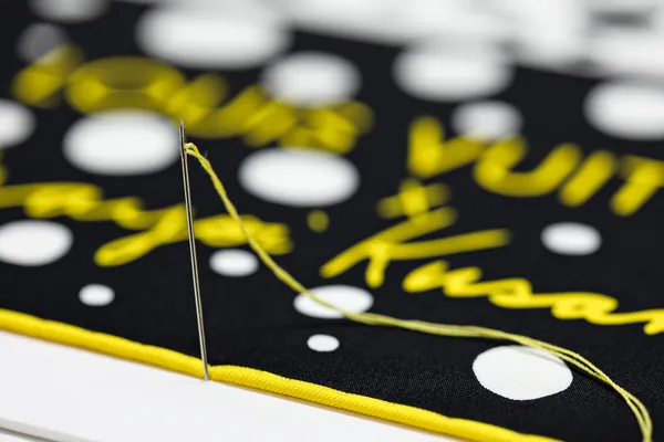 A needle and yellow thread stitching the scarf's edge