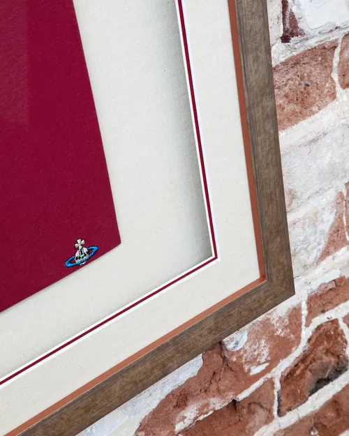 The corner of the frame on a brick wall: silver moulding, linen mount and red inner line
